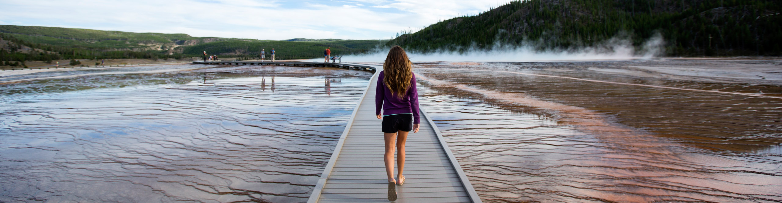 A young female hiking along a boardwalk over geothermal hot springs in Yellowstone National Park.