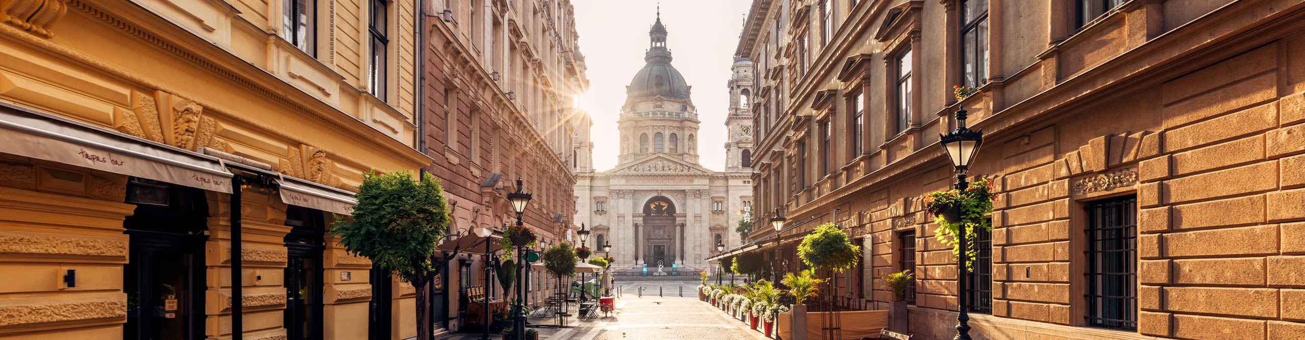 Pedestrian street in Budapest old town leading to St Stephen's Basilica, with sun setting behind 