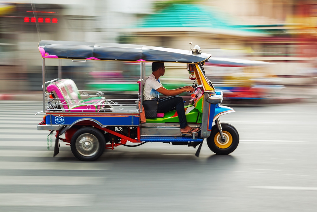 Colourful tuk-tuk zipping in between traffic on a busy Bangkok streets, Thailand on an Intrepid Travel tour