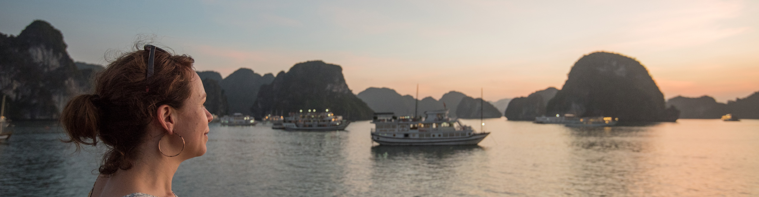Woman looking at sunset over the islands and boats of Halong bay, Vietnam