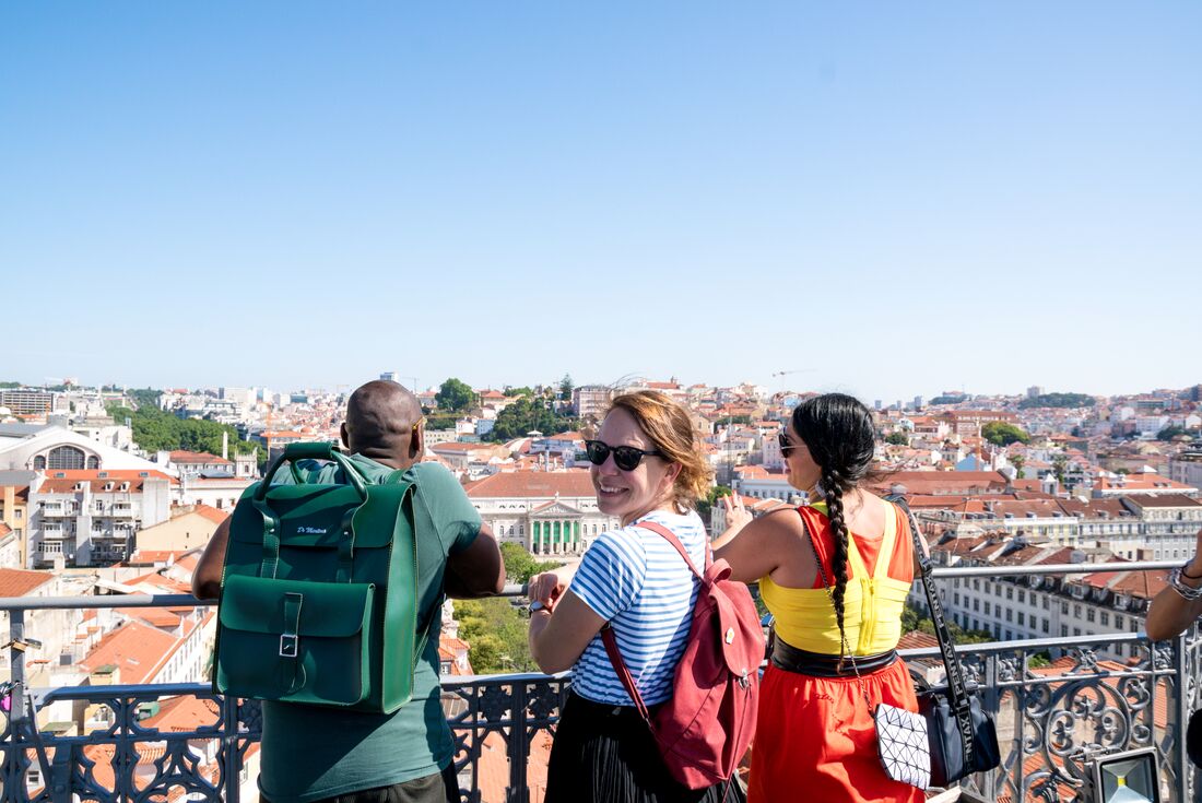 A group of three travellers stand on a balcony overlooking the city in Lisbon, Portugal