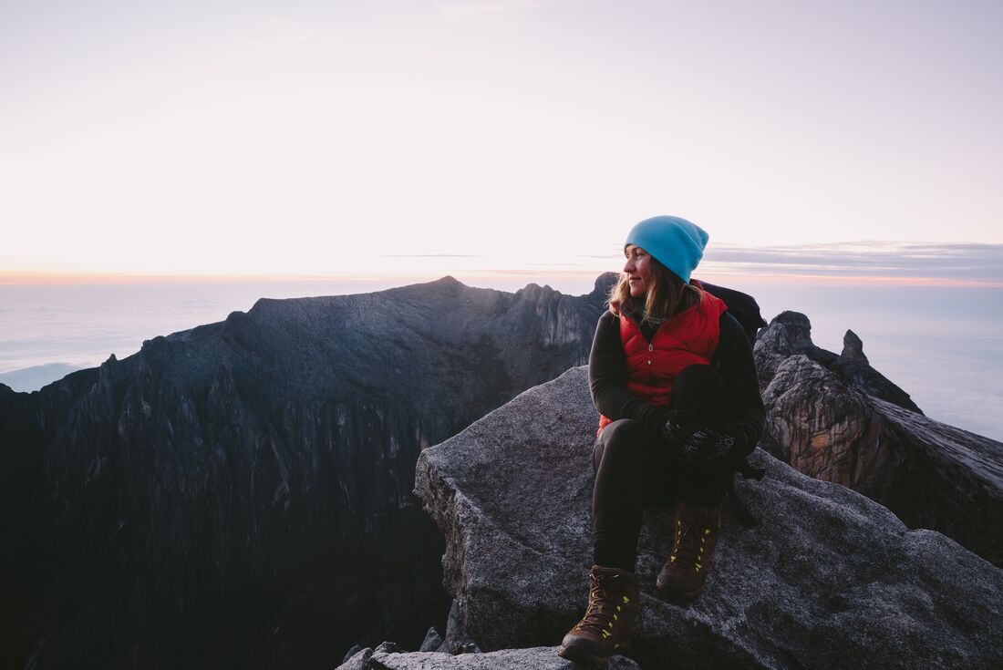 Female traveller in warm clothes sitting at the summit of Mount Kinabalu at sunrise in Borneo