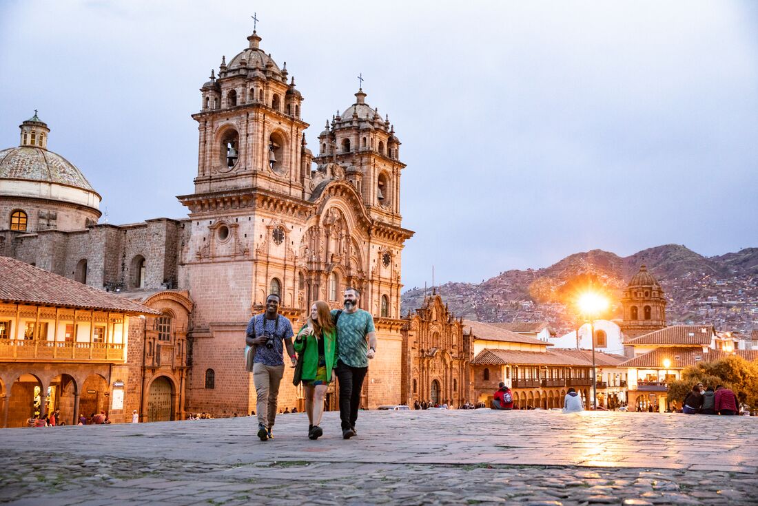 A group of three people walk away from Cusco Cathedral, they are all smiling and two of them have their arms around each other
