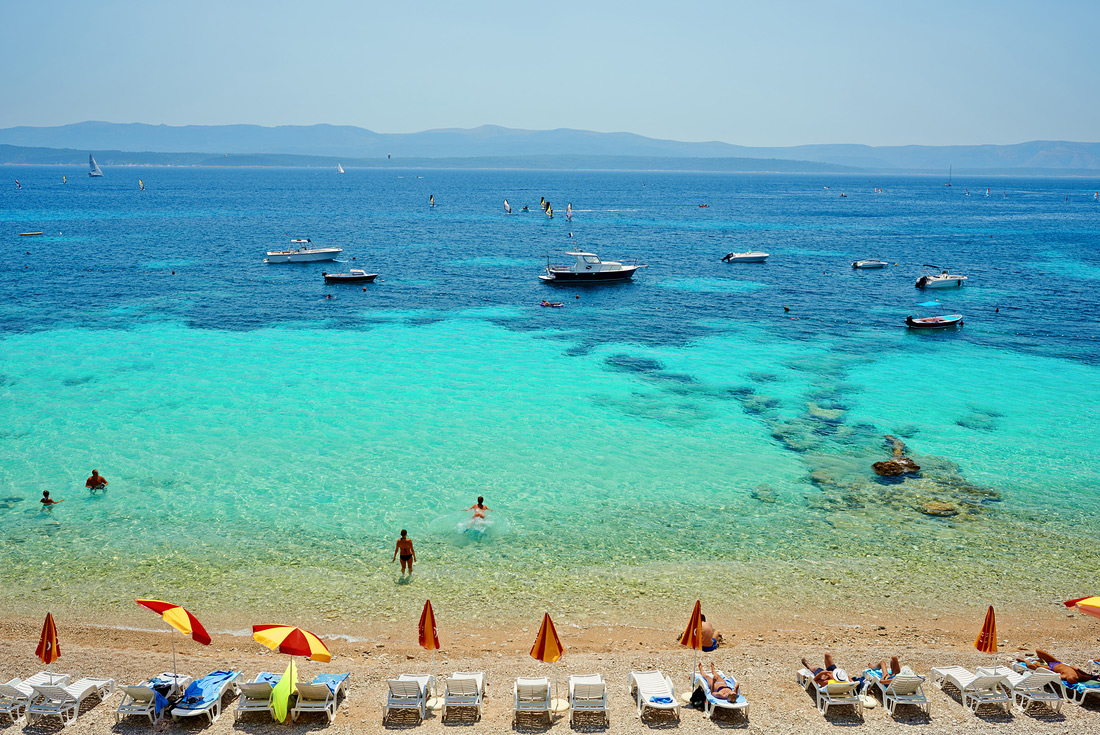 Deck chairs on beach with view of boats and ocean, Brac Island, Croatia