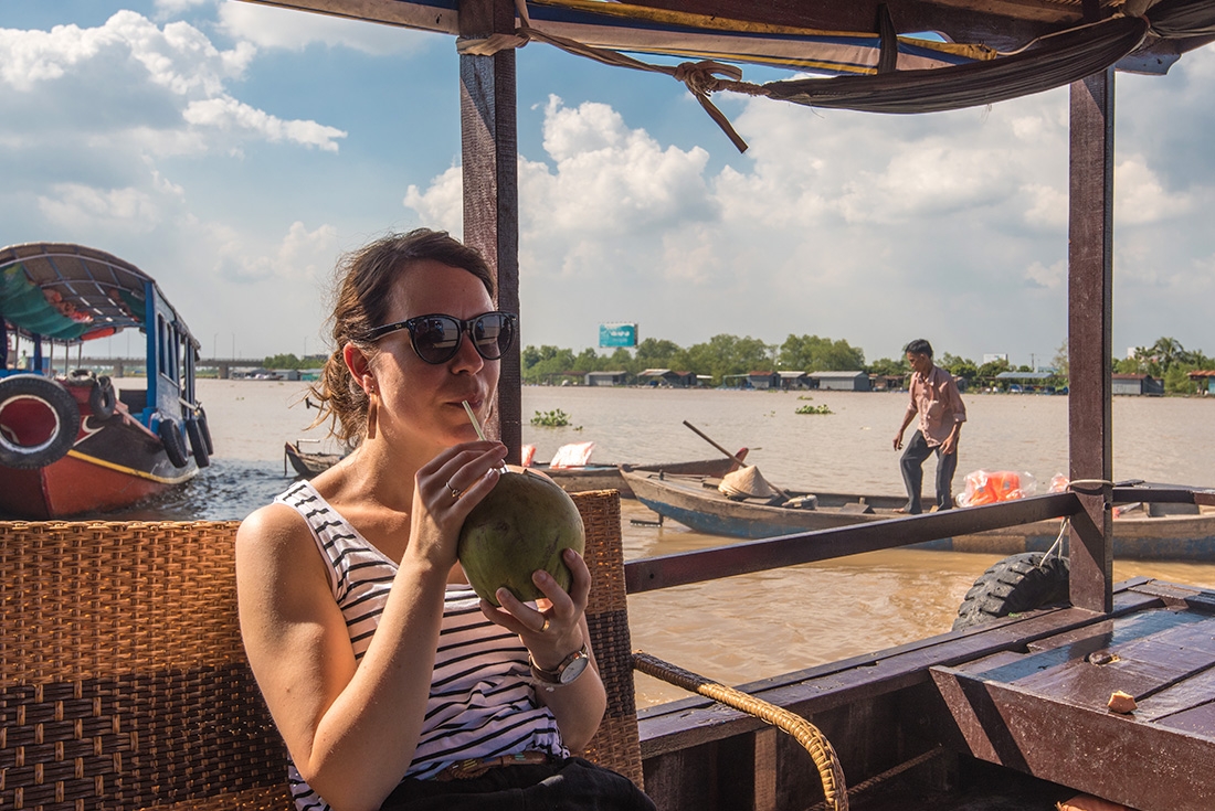 Traveller taking in the sights of the Mekong River via river cruise while drinking from a fresh coconut on an Intrepid Travel Tour.