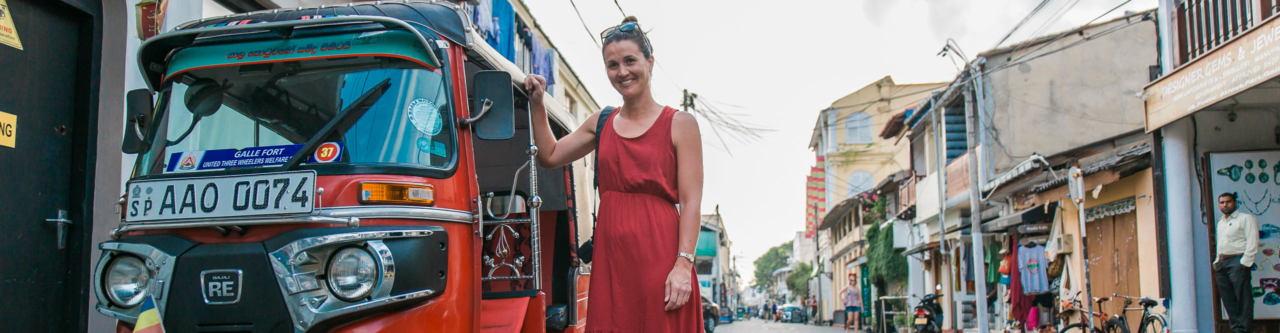 Woman in red dress standing next to a tuk tuk taxi in Sri Lankan street 