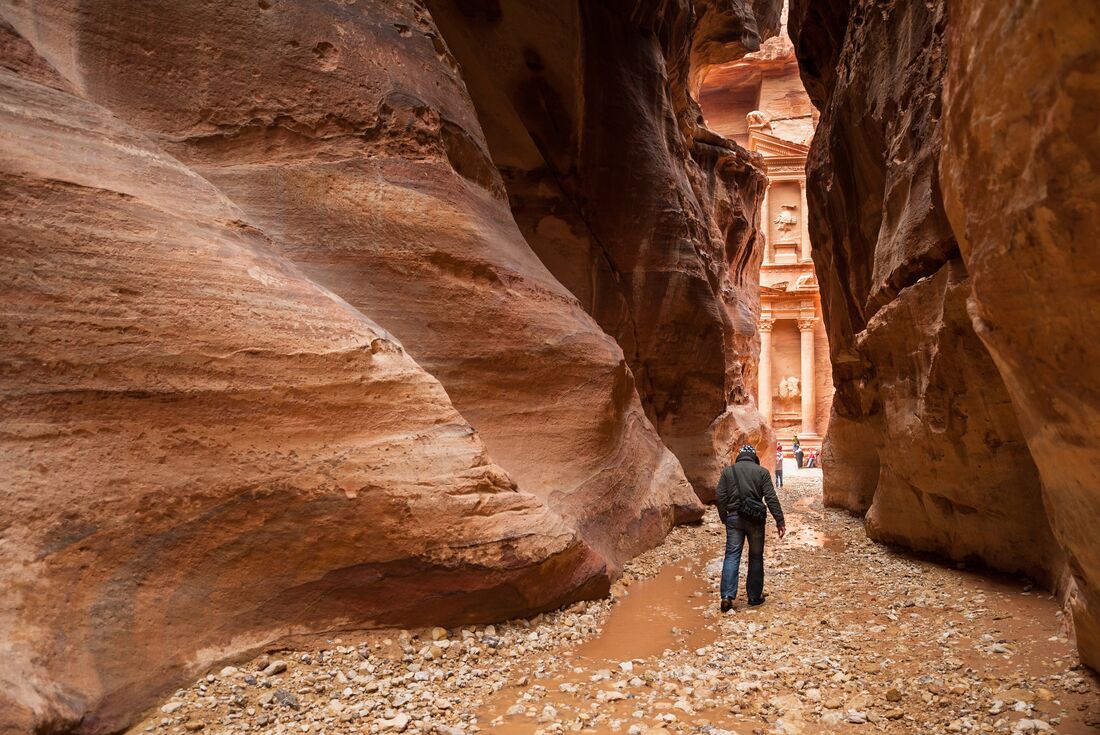 Traveller walks between slim walls of gorge with view of petra at the end