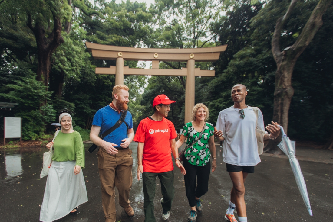 Intrepid leaders and travellers walking around Meiji Jingu temple smiling and laughing in light rain