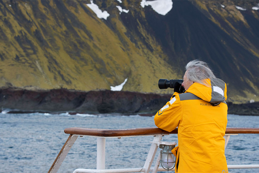 Travellers photographing the rocky green coast of Jan Mayen island