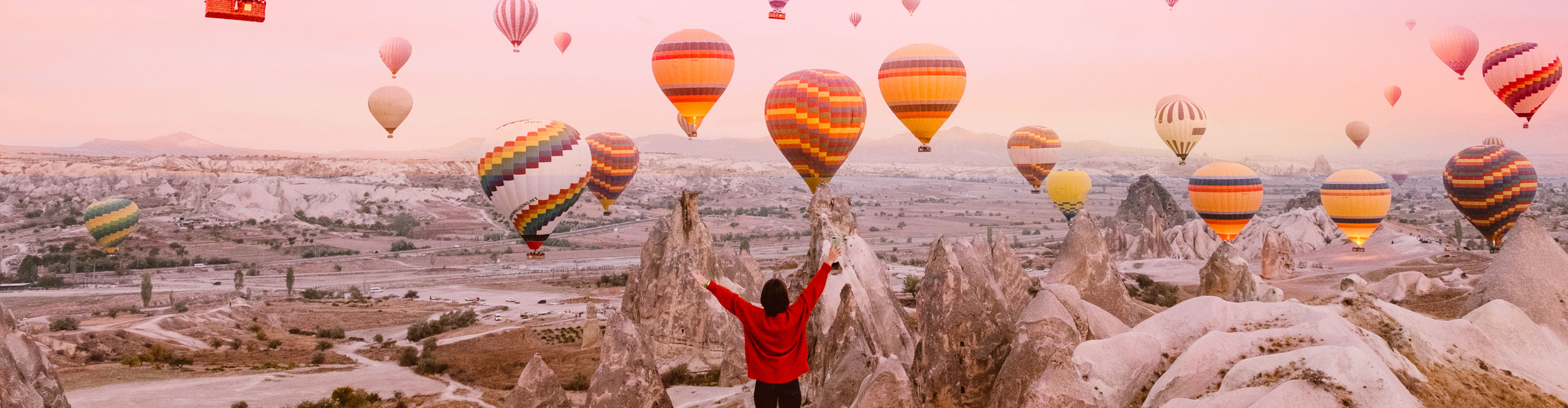 Young woman on a background of flying balloons at sunrise in Cappadocia with a pink sky 