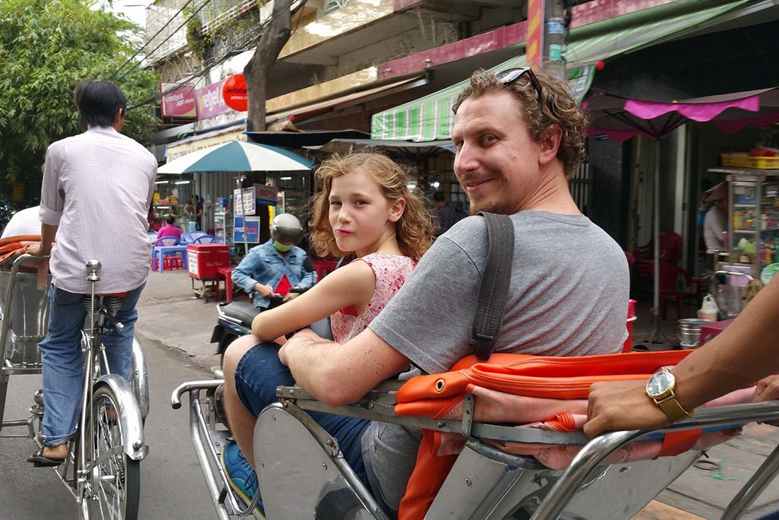 Father and daughter travelling on a rickshaw down a busy Hanoi street on an Intrepid Travel tour.