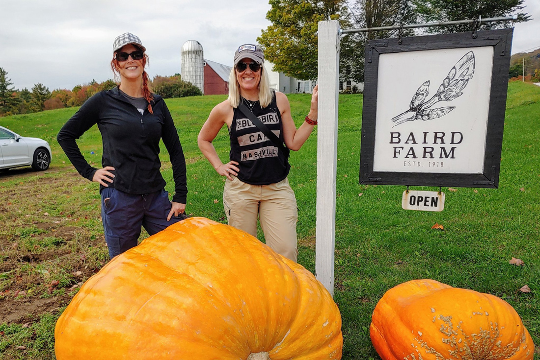 Happy hikers pose for a photo besides large pumpkins and sign in Vermont, USA