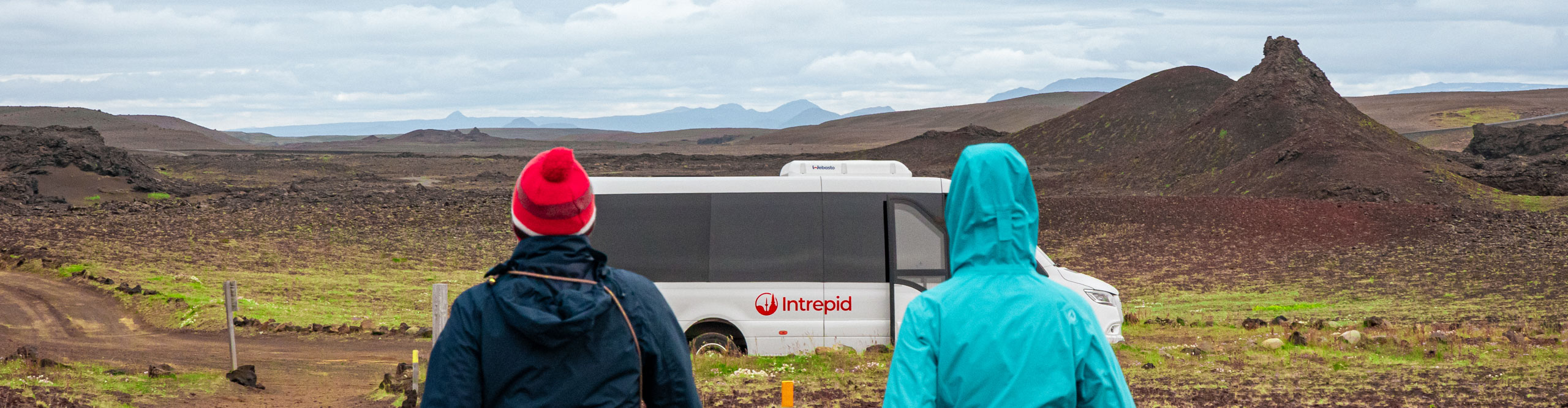 View of the Icelandic landscape with Intrepid tour bus and two travellers in view 