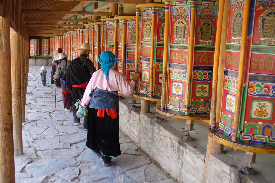 Travellers and pilgrims run their hands over prayer wheels at a Tibetan Monastery