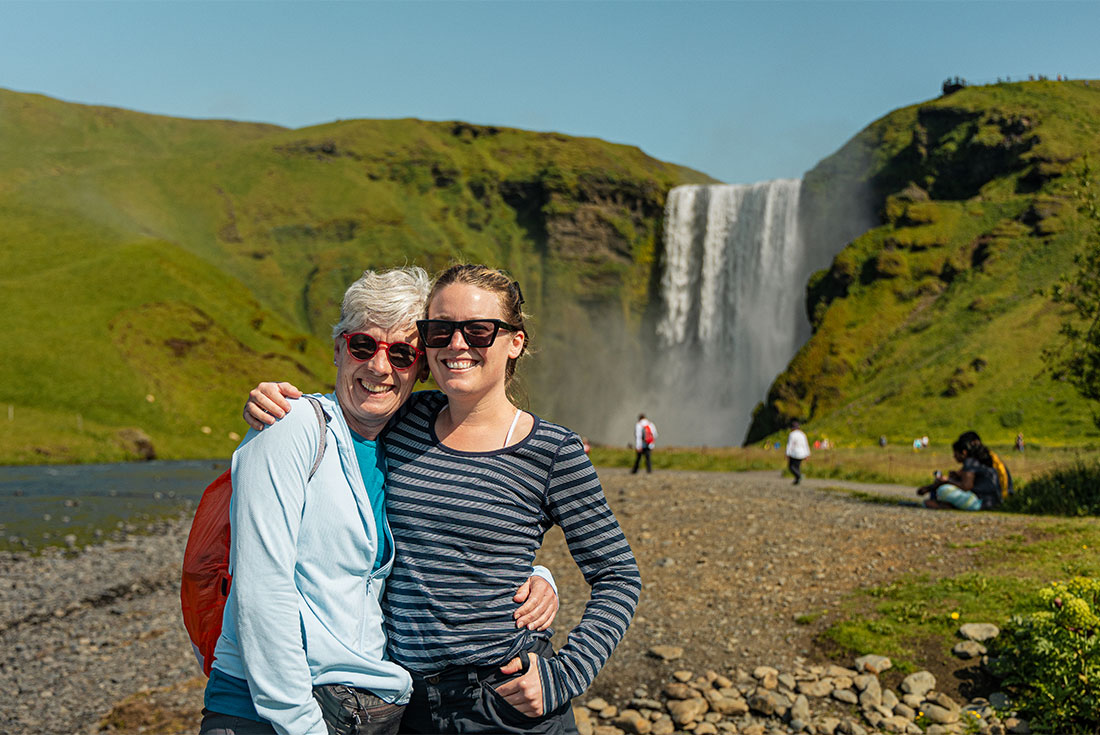 Two travellers stand in front of Skógafoss waterfall in Iceland's south coast