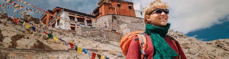 Traveller with backpack and sunglasses standing in front of Tibetan monastery and prayer flags