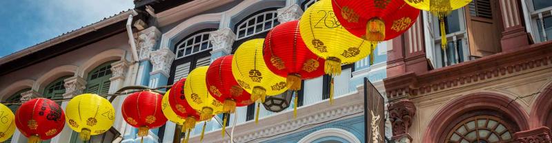 Red and yellow lanterns hang outside colourful buildings in Chinatown, Singapore
