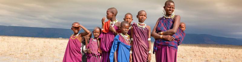 A masai family in traditional robes standing in the middle of the serengeti with mountain range in the background