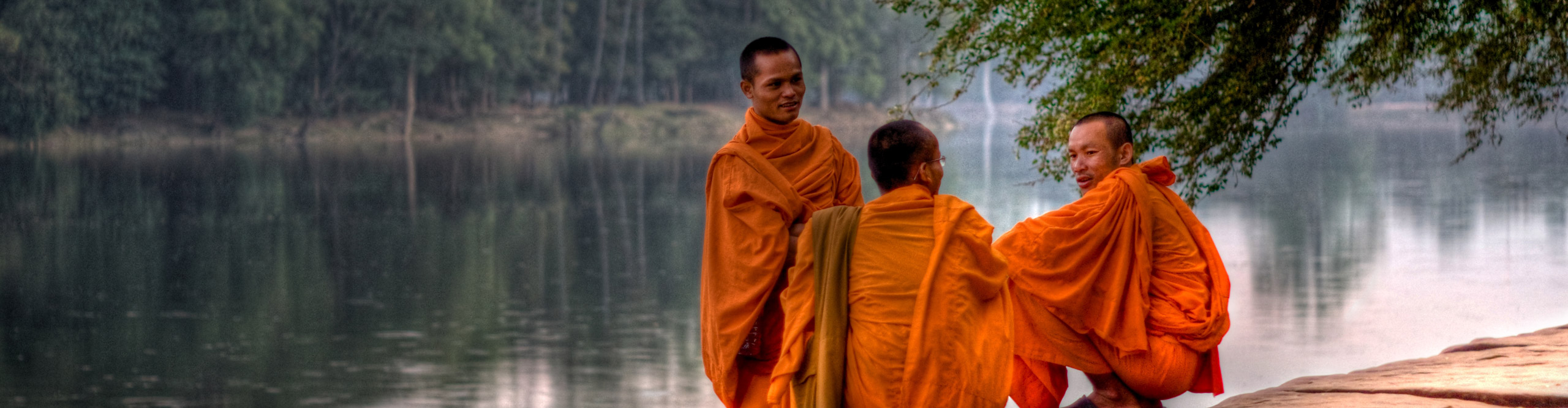 Monks in orange robes talking and laughing by the river at sunset near Siem Reap, Cambodia 