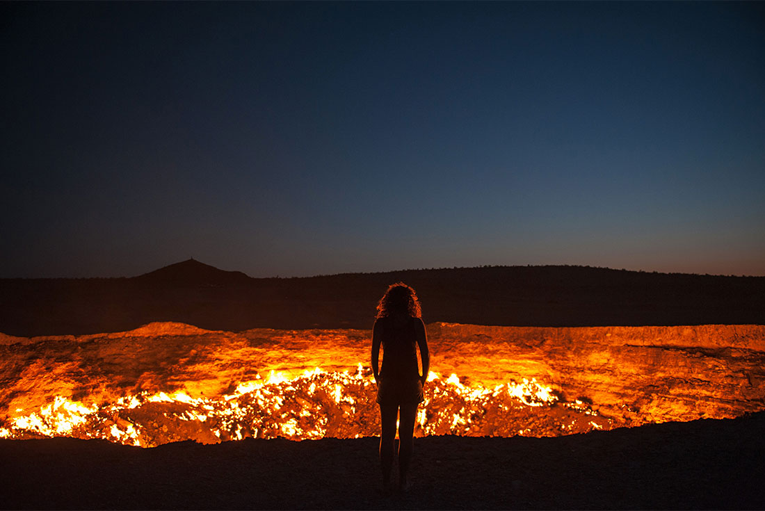 Intrepid Traveller stands before the constantly burning crater of Darvaza at night in Turkmenistan