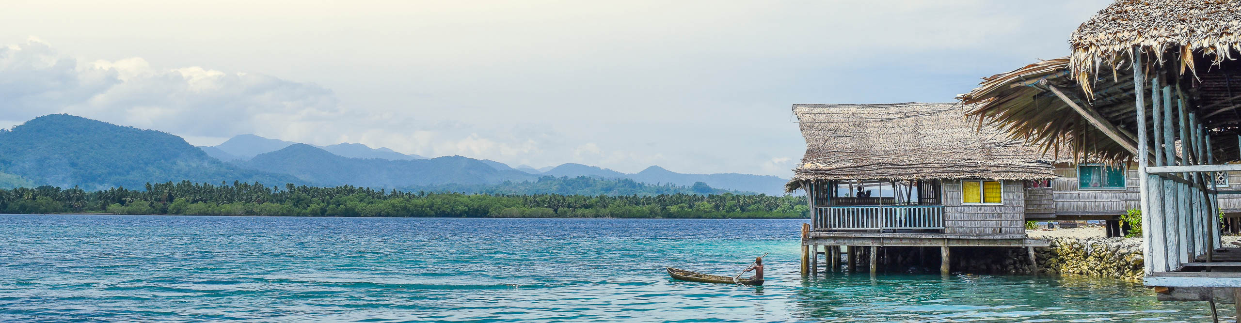 Fisherman on boat next to hi stilt house on the water in the Solomon Islands