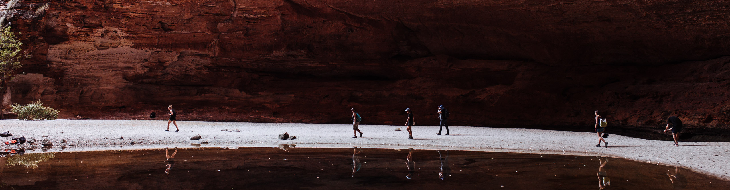 Hikers walking near the water through the red rock of the gorge at the Kimberley, Western Australia 