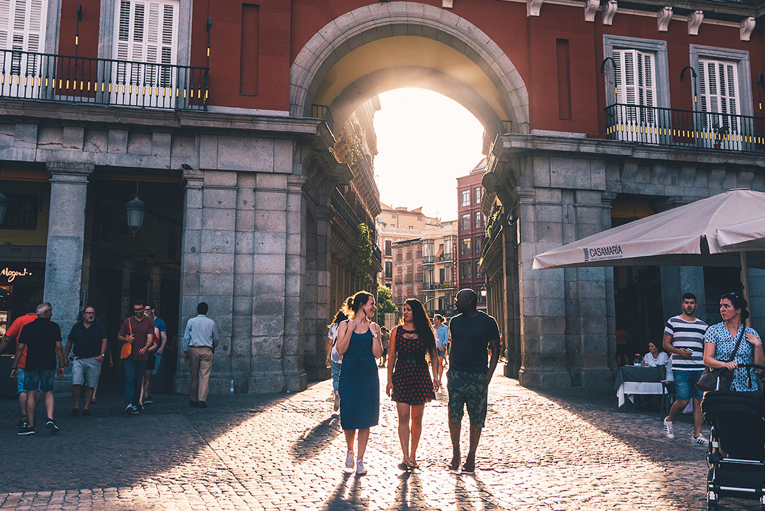 Intrepid travellers walk cobbled city street of Madrid with sunset, Spain