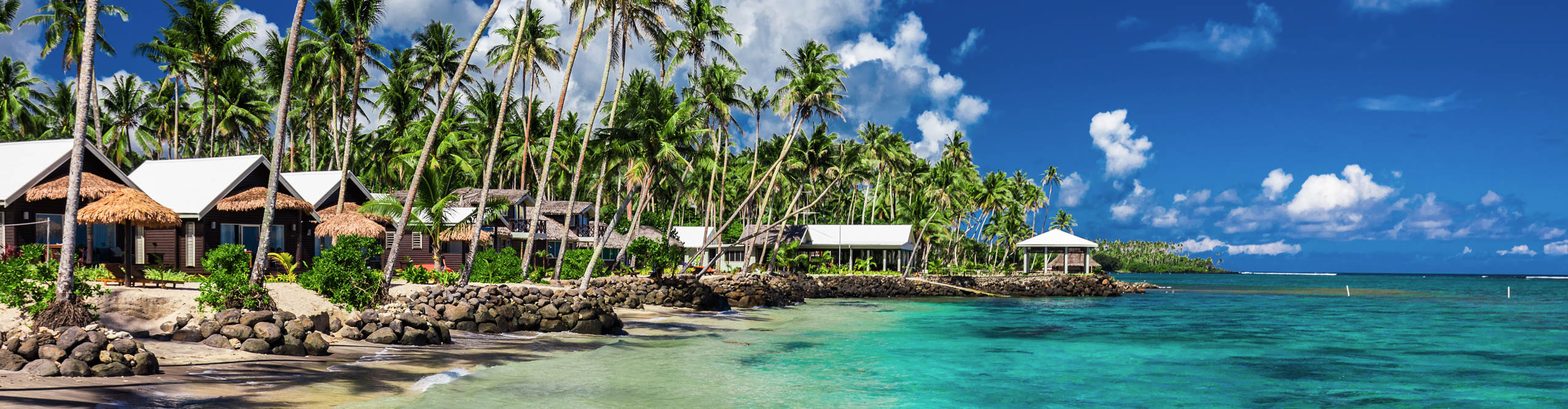 Tropical beach with with coconut palm trees, turquoise water and villas on Samoa Island, with 