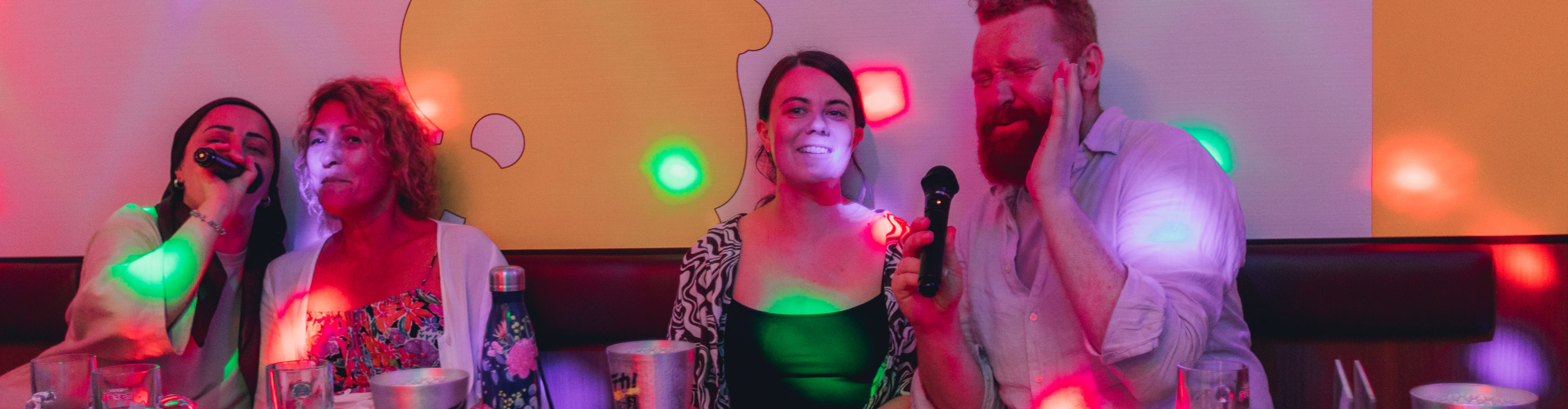 Group singing in a karaoke booth with brights coloured lights on the wall, Osaka, Japan