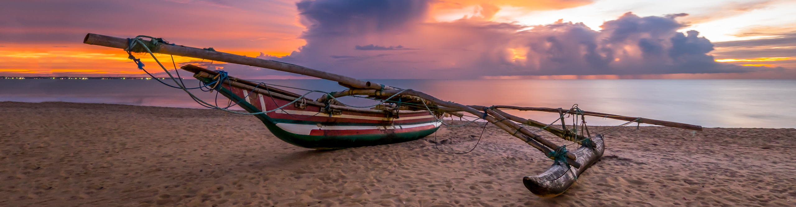 Traditional wooden fishing boat on the beach at sunset with a bluey pink sky in Negombo, Sri Lanka