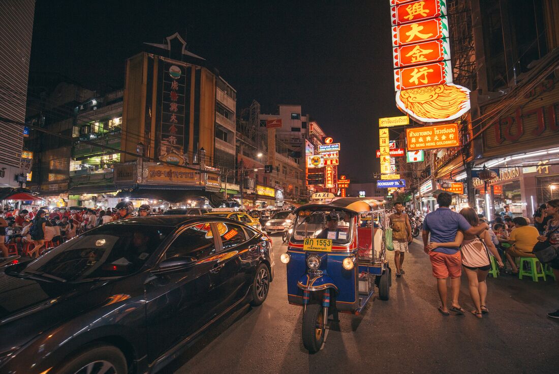 Tuk tuk and cars on the rooad and people filling the streets at night in Bangkok.