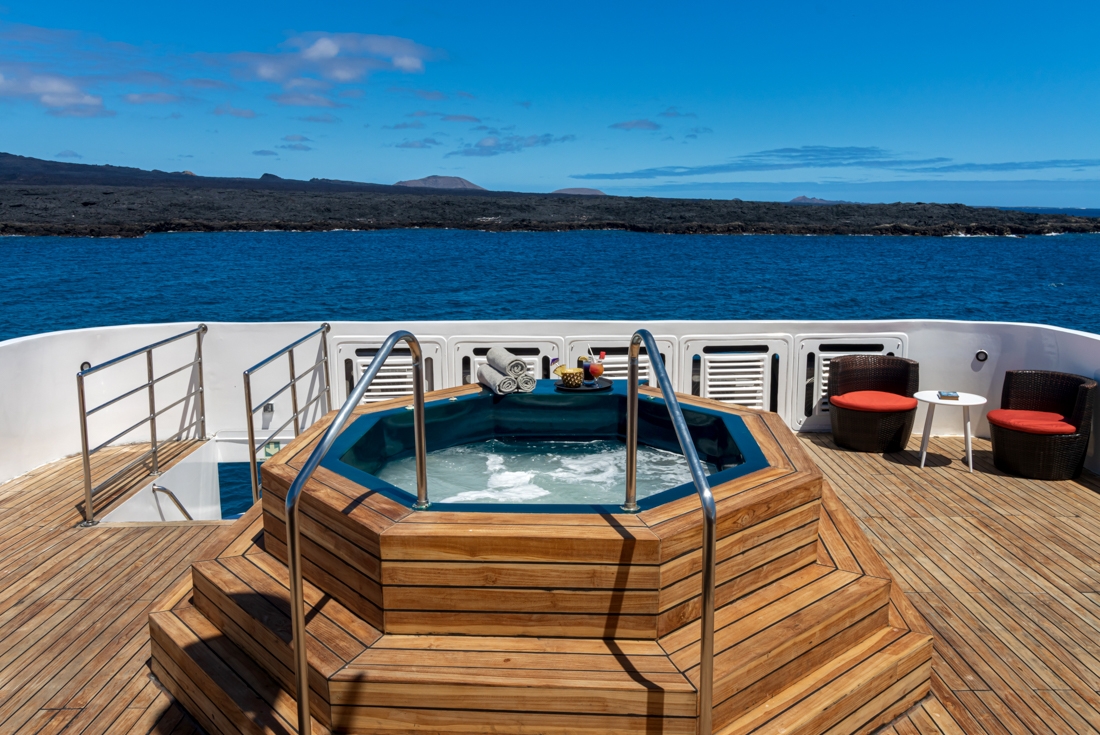 Back deck of the Grand Queen Beatriz with a hot tub and drinks ready, Galapagos Island visible on horizon