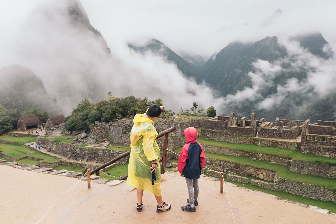 Mother and daughter wearing raincoats as they look out over Machu Picchu 