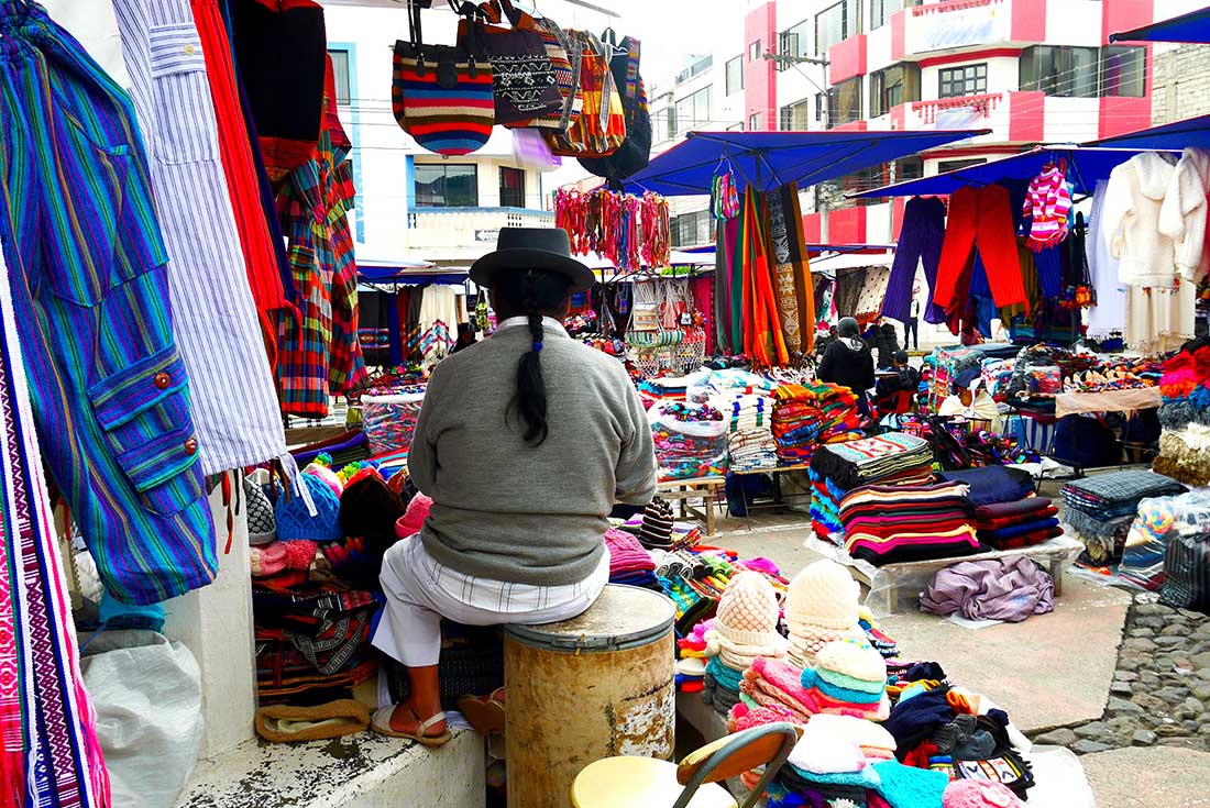 Local person sitting at a stall surrounded by traditional Ecuadorian clothes at Otavalo Market