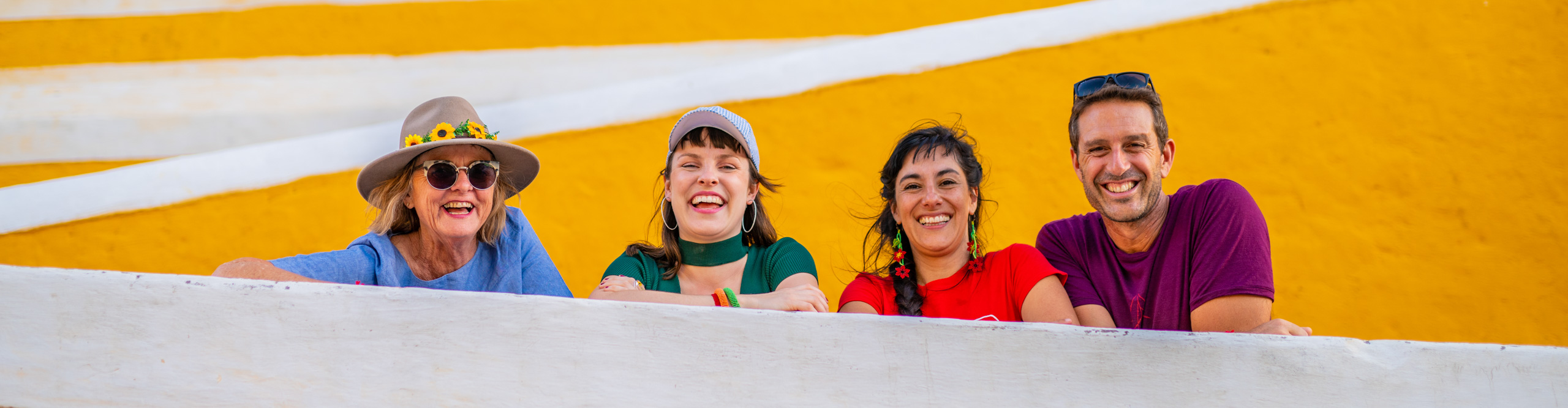 Travellers laughing and smiling leaning on a yellow wall in the the yellow city in Izamal, Mexico