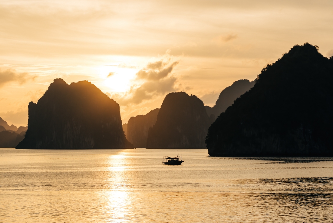 Halong Bay.at sunset with a fishing boat cutting across the water
