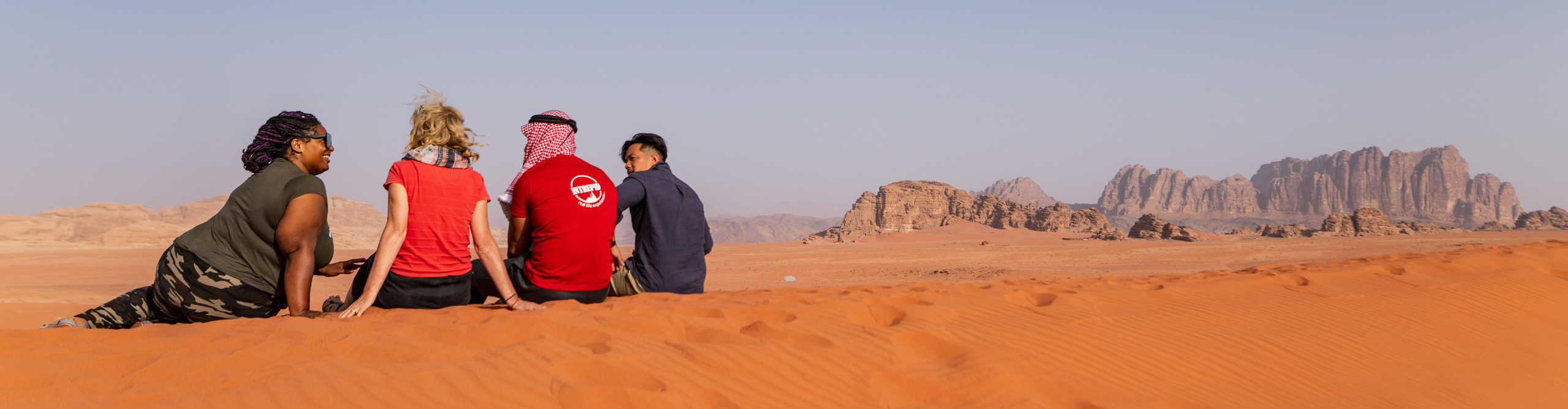Travellers sitting on sand dune, Wadi Rum Jordan