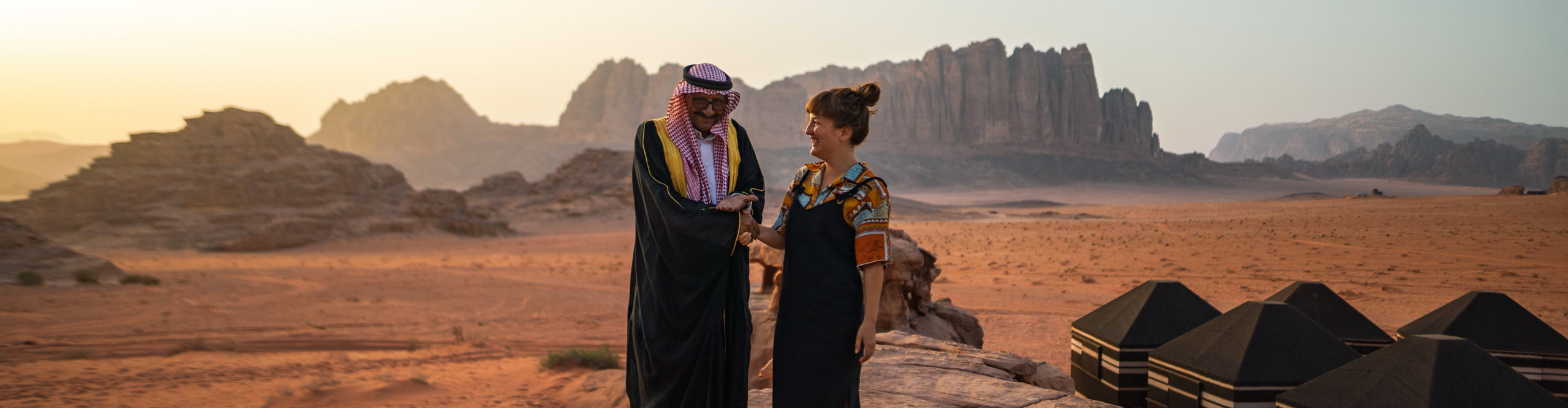 Woman laughing, with guide, wearing traditional middle eastern clothes in the desert at sunset