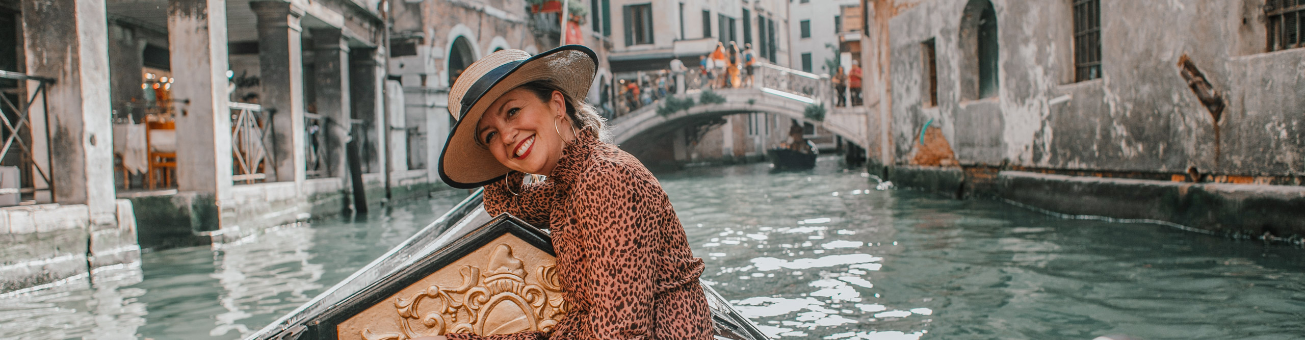 Woman smiling wearing a dress and hat on a gondola in Venice 