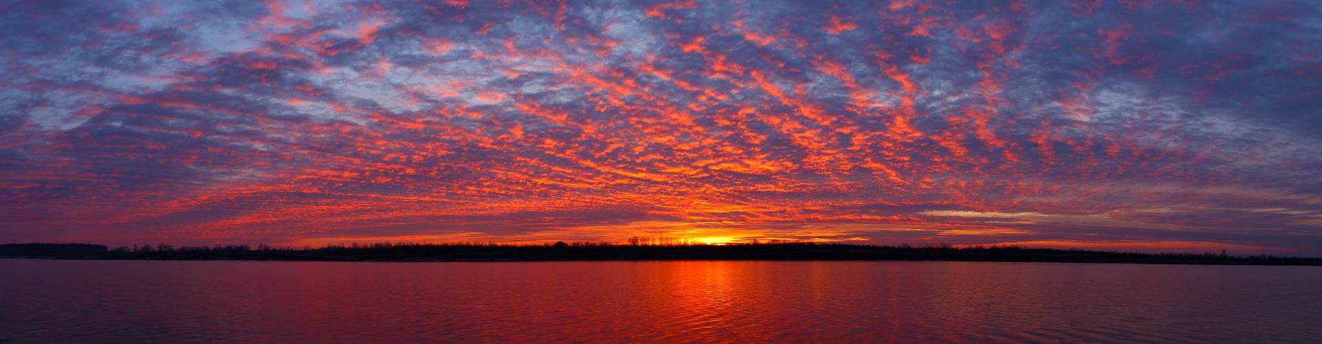 A twilight sky awash with purple, orange and yellow as the sun sets over a lake 