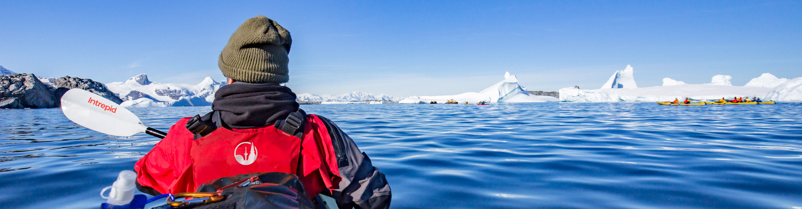 Person I waiting Intrepid jacket kayaking in the bright sun near icebergs, Antarctica 
