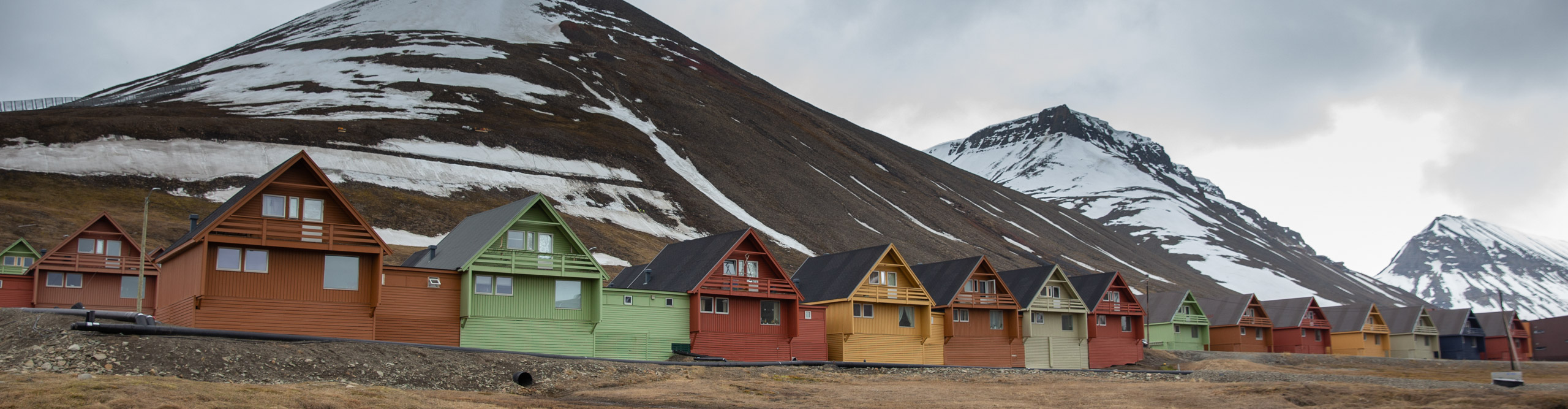 Buildings on shoreline with snowy mountains behind in the Arctic on a cloudy day
