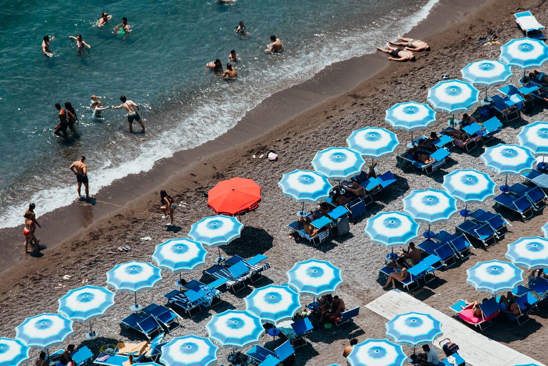 Uniform blue and white umbrellas dot the black sand beach of Minori town on the Amalfi Coast