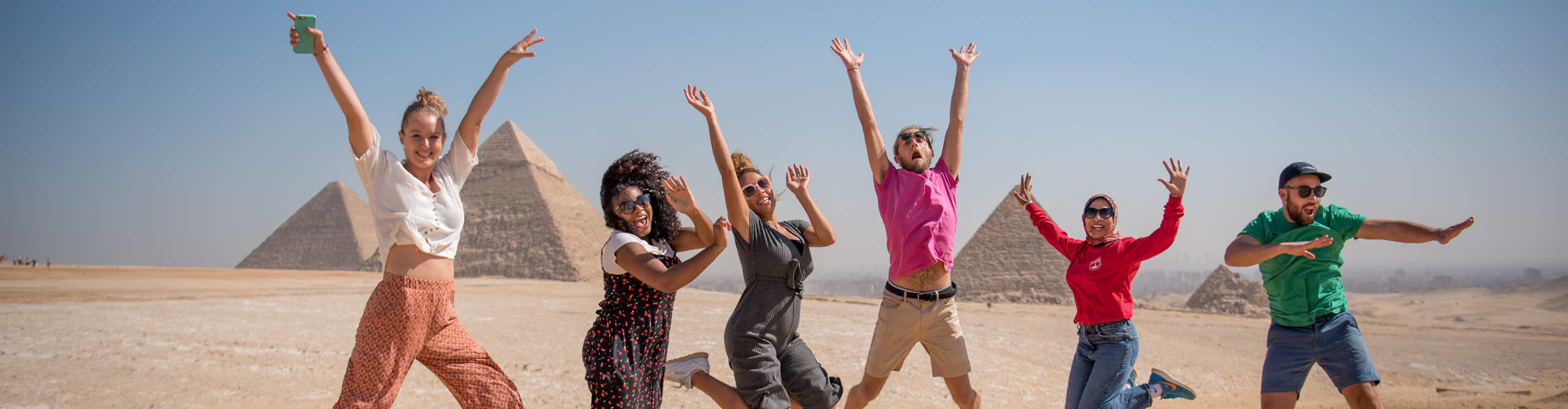 Group leaping in the air in front of pyramids with hands in the air on a clear sunny day, Egypt