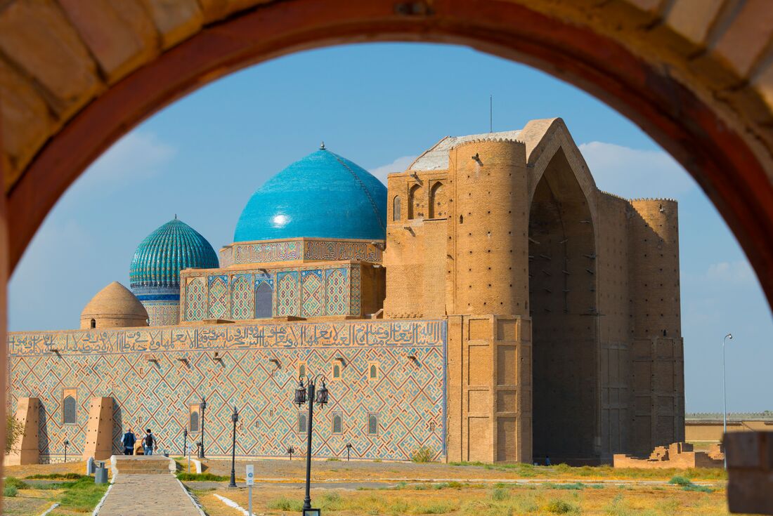 The cerulean domes of  Khoja Ahmed Yasawi Mausoleum visible through a sandstone arch, Turkistan, Khazakhstan
