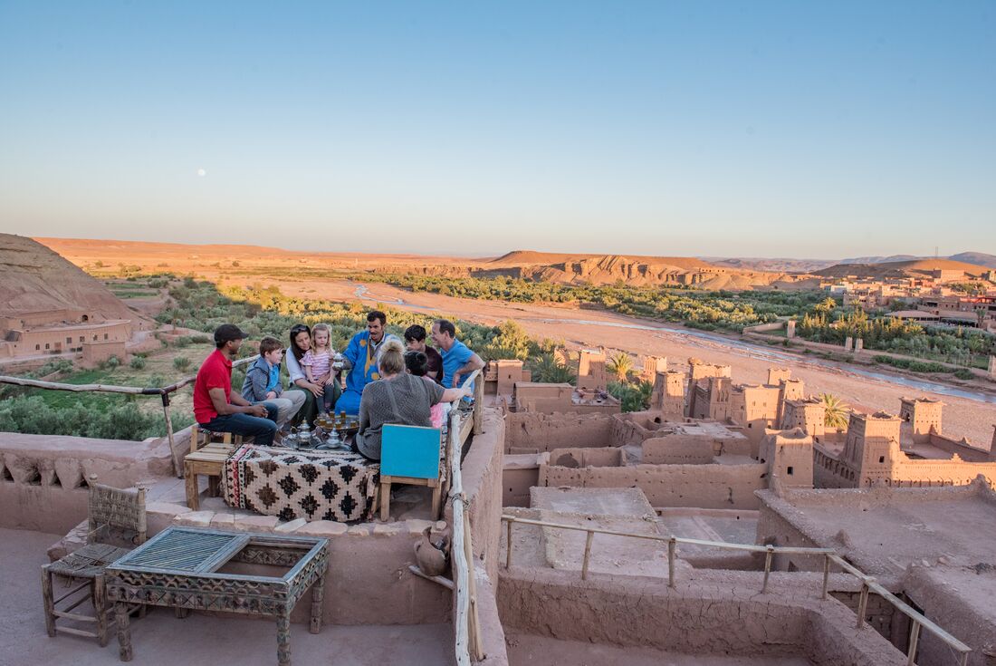 Group of Intrepid family travellers share a meal on a balcony overlooking the landscape around Ait Benhaddou