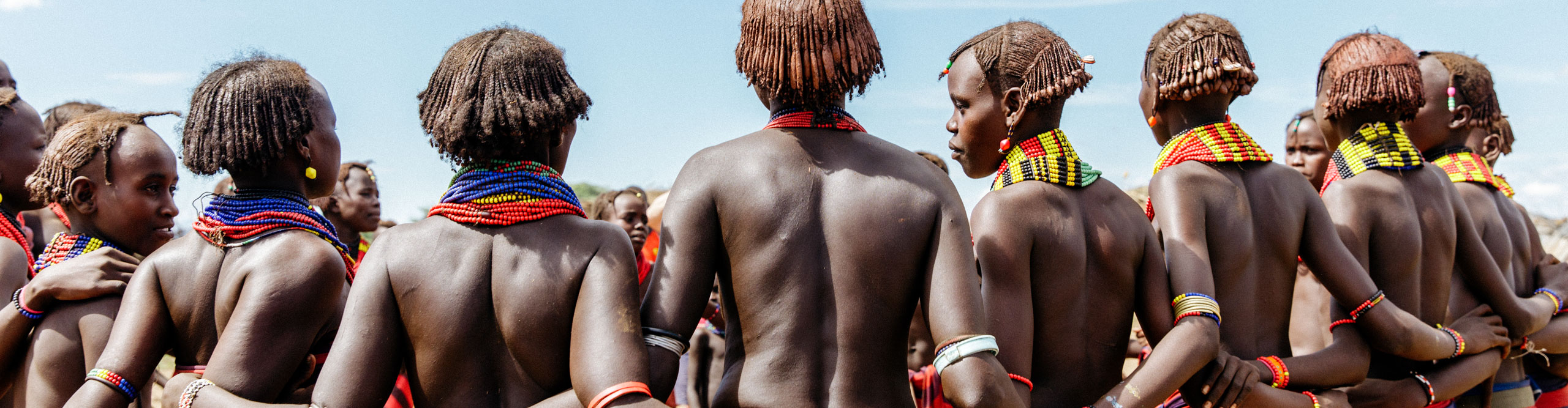 Ethiopian women in tribal dress, with red and black skirts dancing in a circle on a clear sunny day