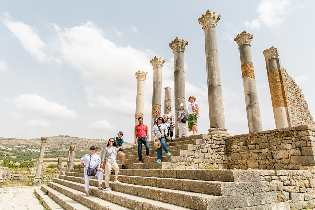 Intrepid Travel group posing with pillars of ruins in Voulibis, Morocco
