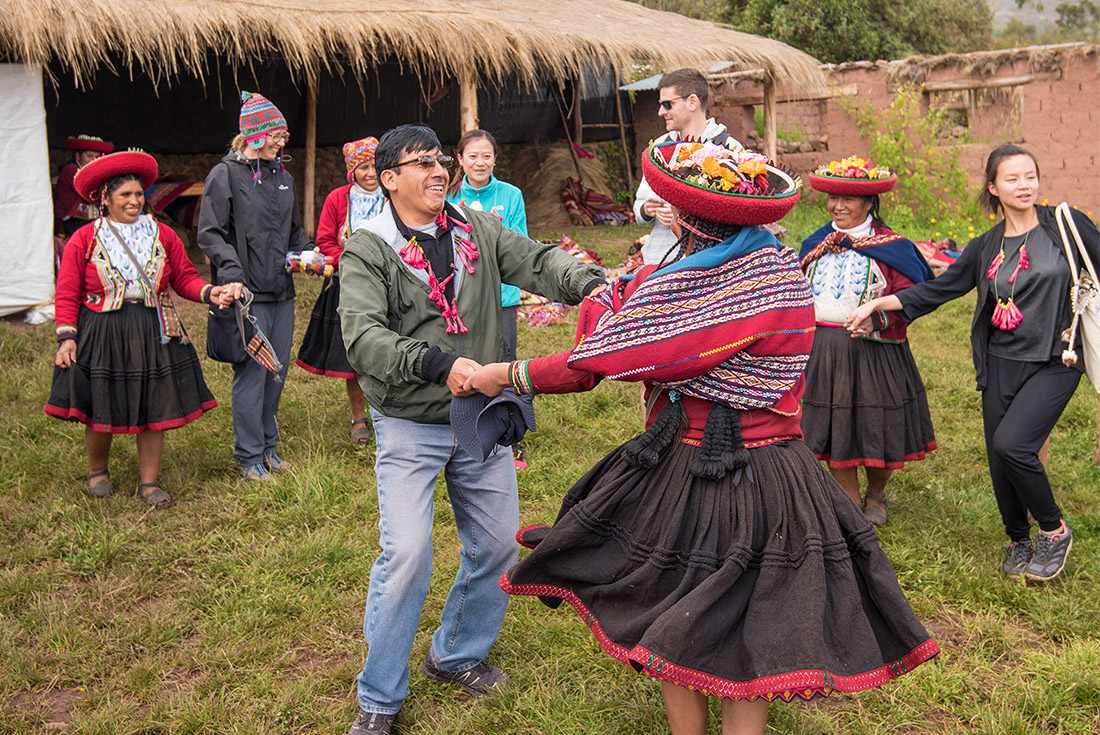 Group of travellers and locals dancing in traditional dress, Sacred Valley community visit, Peru