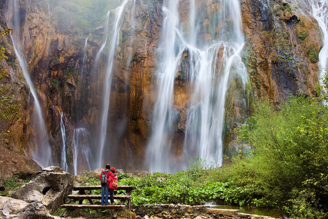 ZMPY - Couple hugging in front of waterfall located in Plitvice Lakes National Park, Croatia